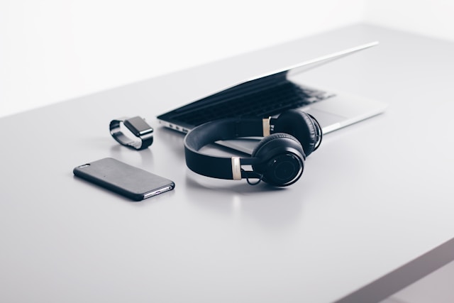 An image of Laptop, Headphones, Mobile phone and a Smart Watch on the table